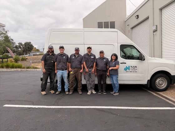 Five workers in uniforms posing beside a white service van outside a warehouse