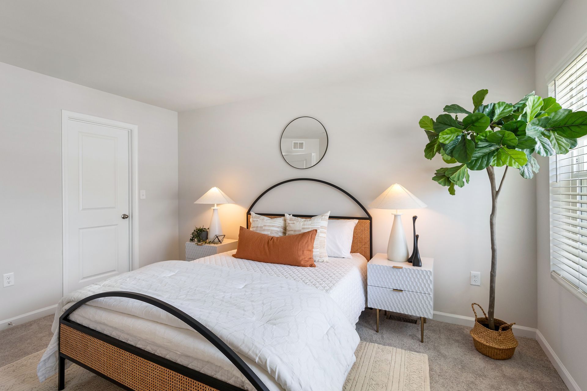 A bedroom with a bed , nightstand , lamps and a plant.