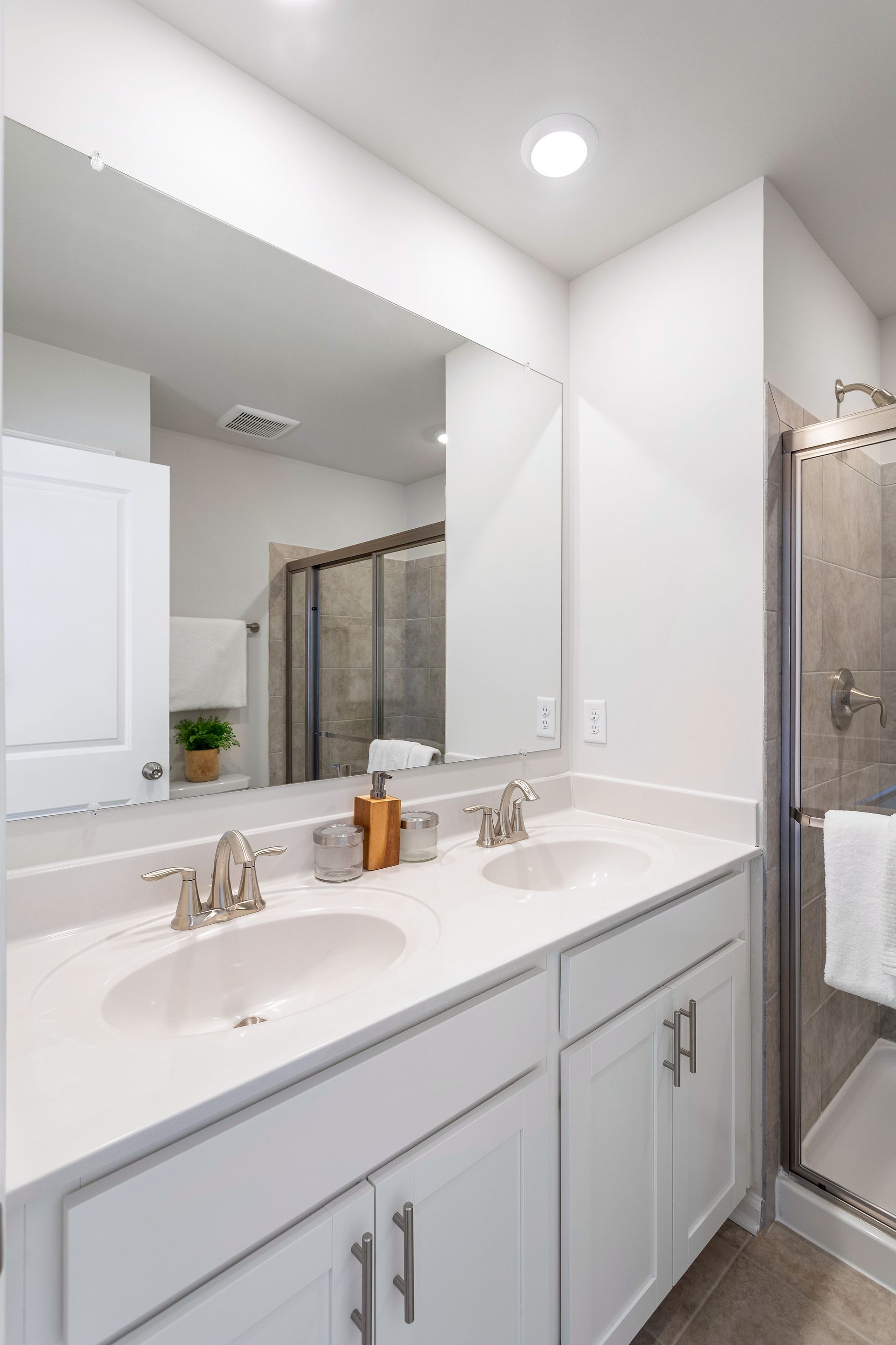 A bathroom with two sinks , a large mirror and a walk in shower.