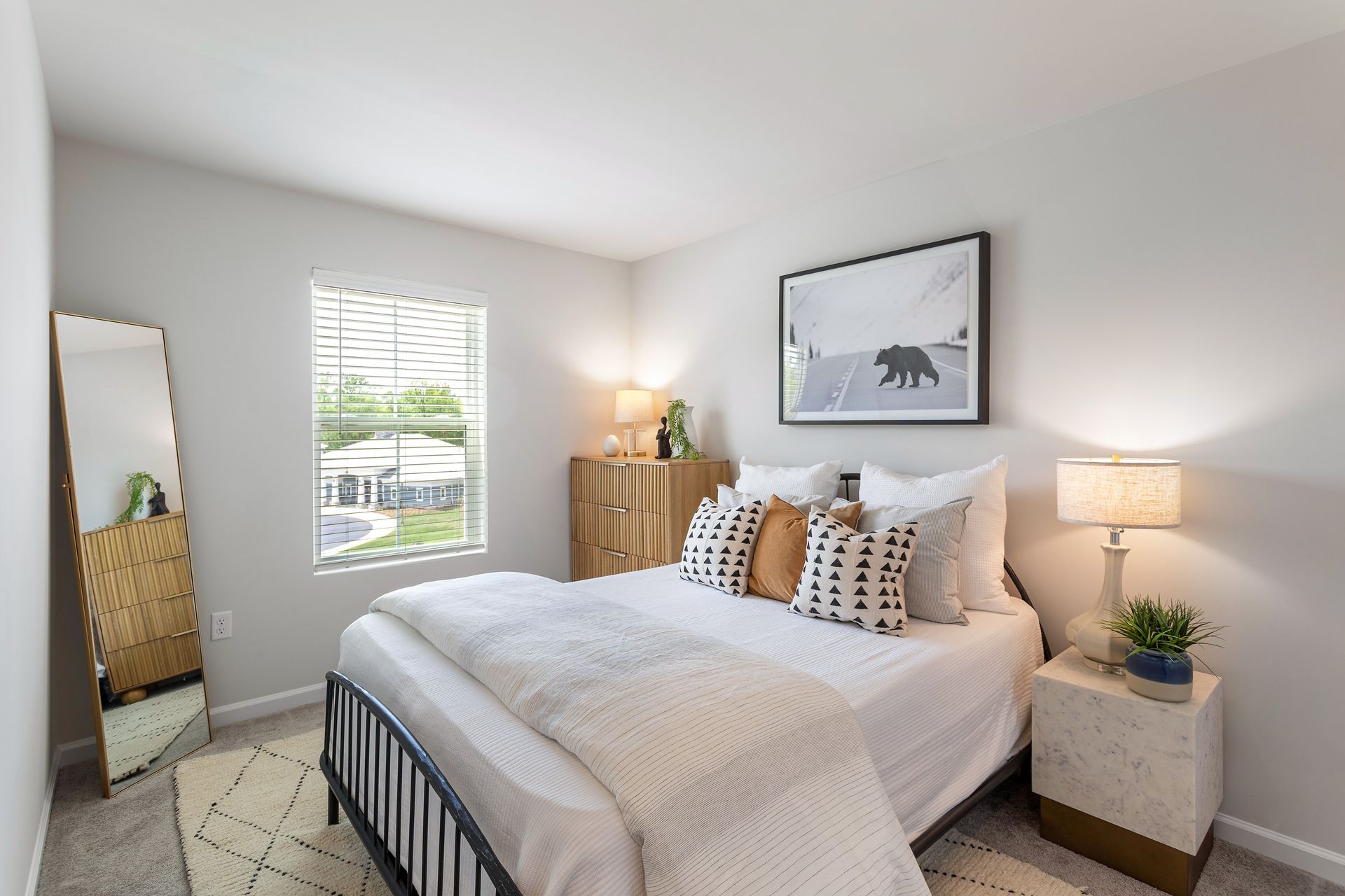 A bedroom with a bed , nightstand , mirror and dresser.