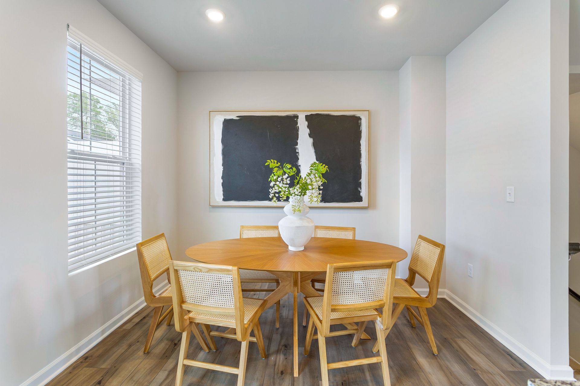 A dining room with a table and chairs and a picture on the wall.