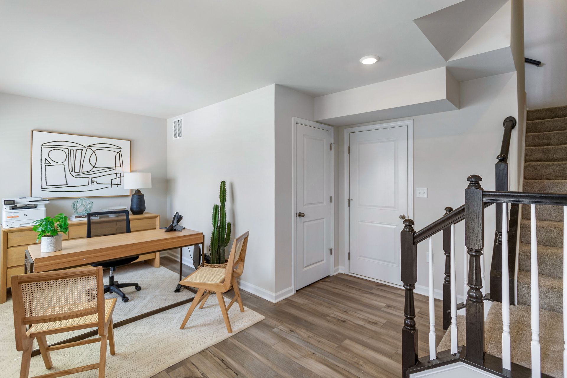 A home office with a desk , chairs and stairs.
