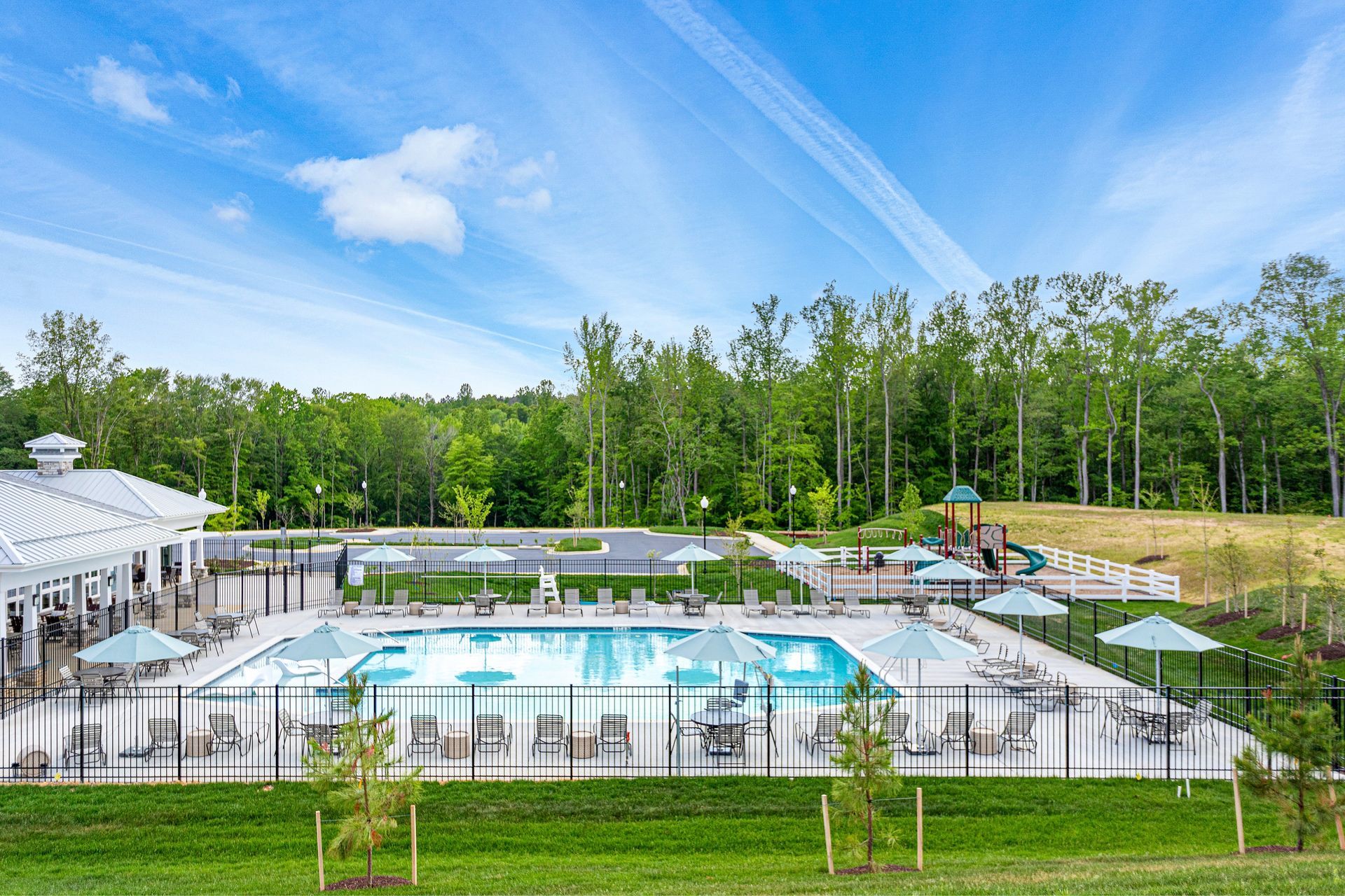 A large swimming pool surrounded by umbrellas and chairs in a park.