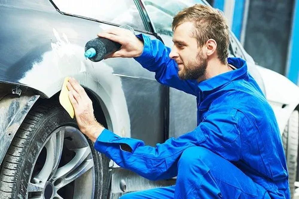 A Man in Blue Overalls is Polishing a Car With a Sponge — Seabreeze Auto Body in Coffs Harbour, NSW