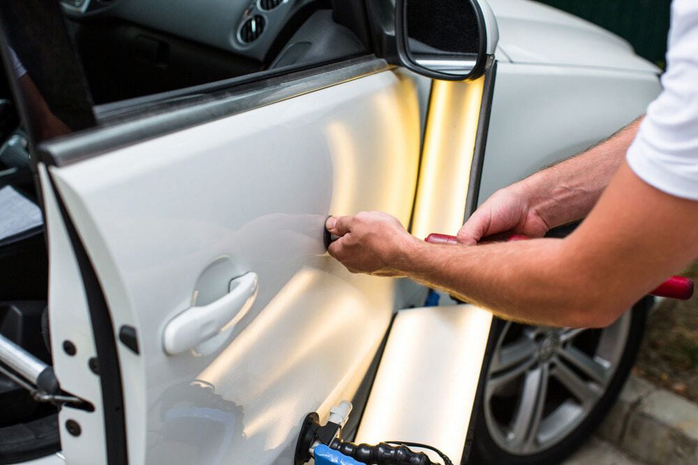 A Man is Repairing a Car Door With a Light — Seabreeze Auto Body in Coffs Harbour, NSW