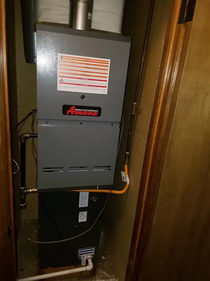 A furnace is sitting in a corner of a room next to a door.