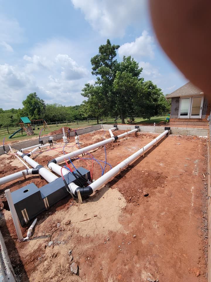 A bunch of pipes are laying in the dirt in front of a house.