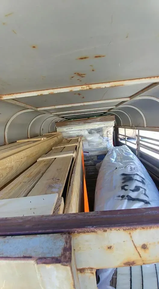 A trailer filled with lots of wooden boards and a boat.