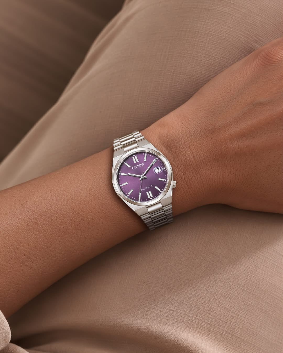 Polso con un orologio d’argento dal quadrante viola, appoggiato su un tessuto beige