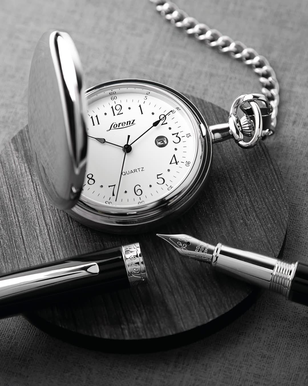 Orologio da tasca con penna su una superficie scura, in bianco e nero
