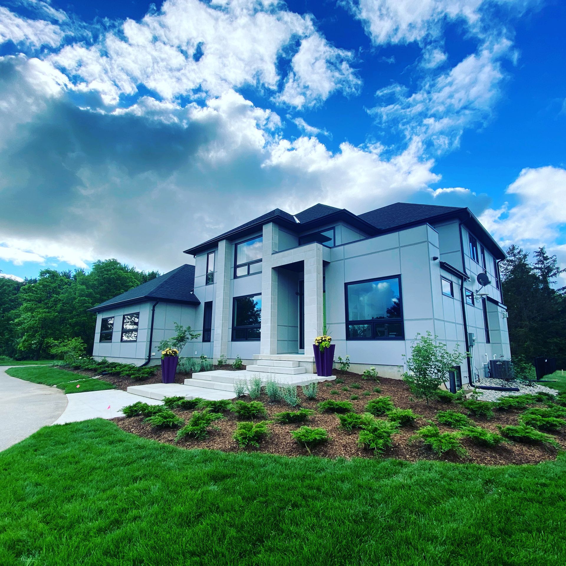 Modern gray house with large windows, bright sky, and lush green lawn.