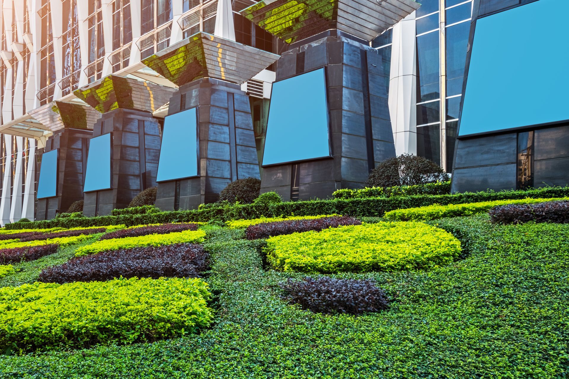 Modern building with tiered green landscaping and blank blue display screens.