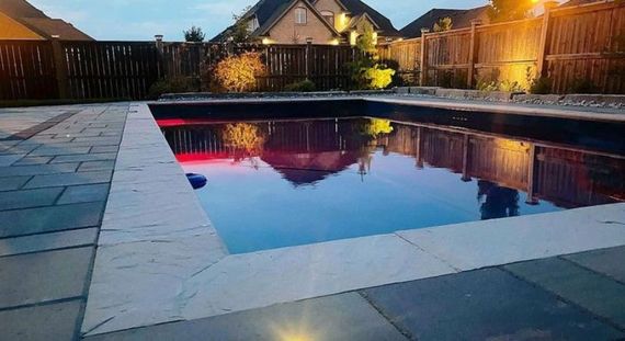 Pool with illuminated red lights reflects surrounding dusk landscape.