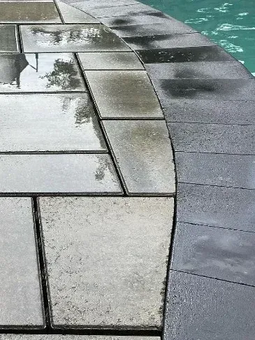 Wet gray paving stones bordering a swimming pool.