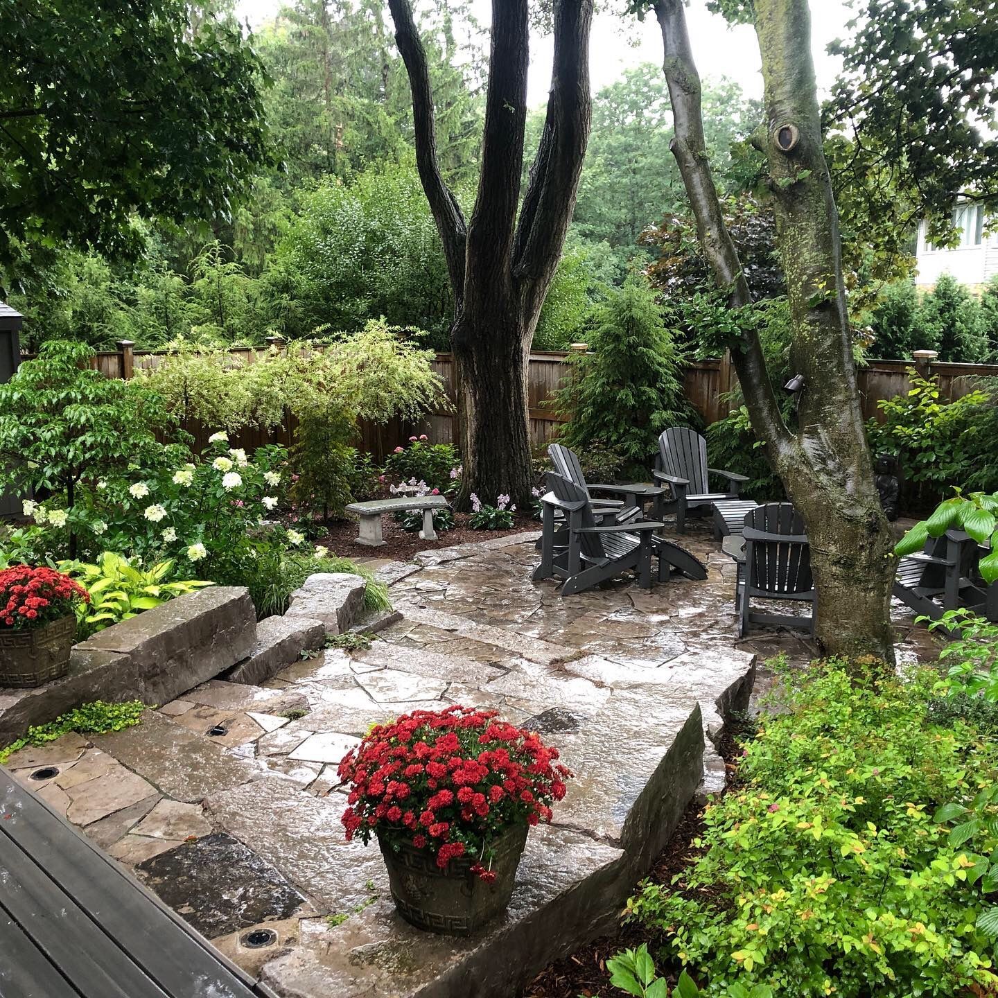 Stone patio with seating area surrounded by lush green garden and trees.