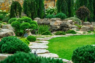 Landscaped garden with layered rocks, lush green plants, and a grassy lawn.