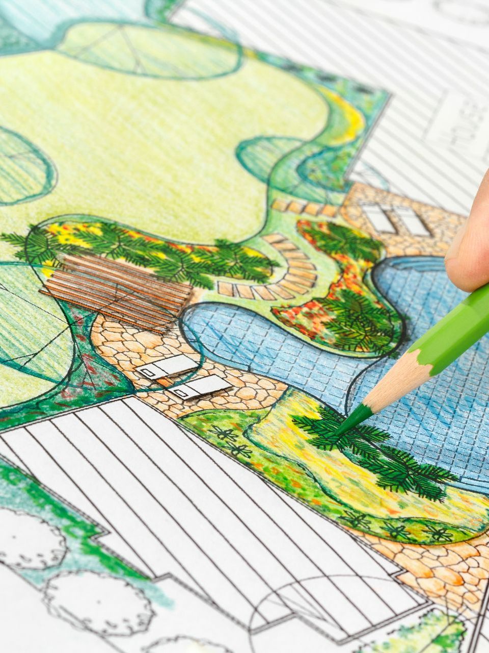 Hand coloring a landscape design with a green pencil, showing a pool, garden, and paved path.