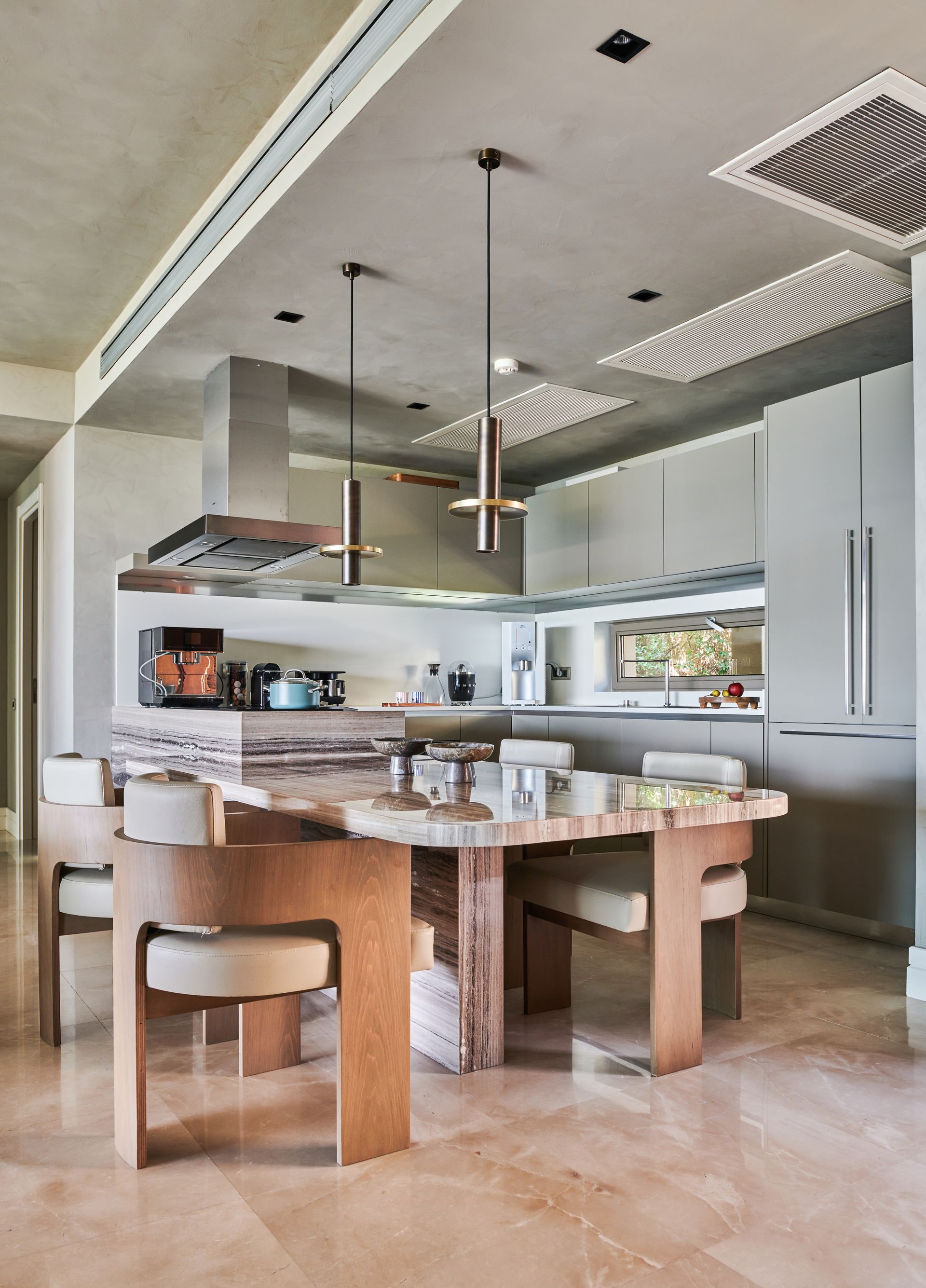 Modern kitchen with a unique stone table, stainless steel hood, and pendant lights.