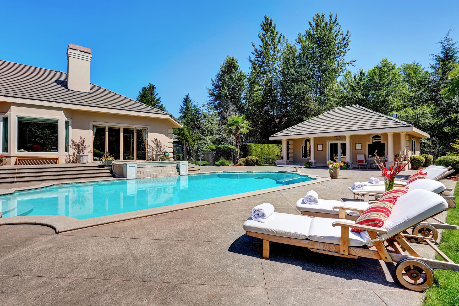 Poolside with lounge chairs, pool, house, and cabana under a sunny, blue sky.