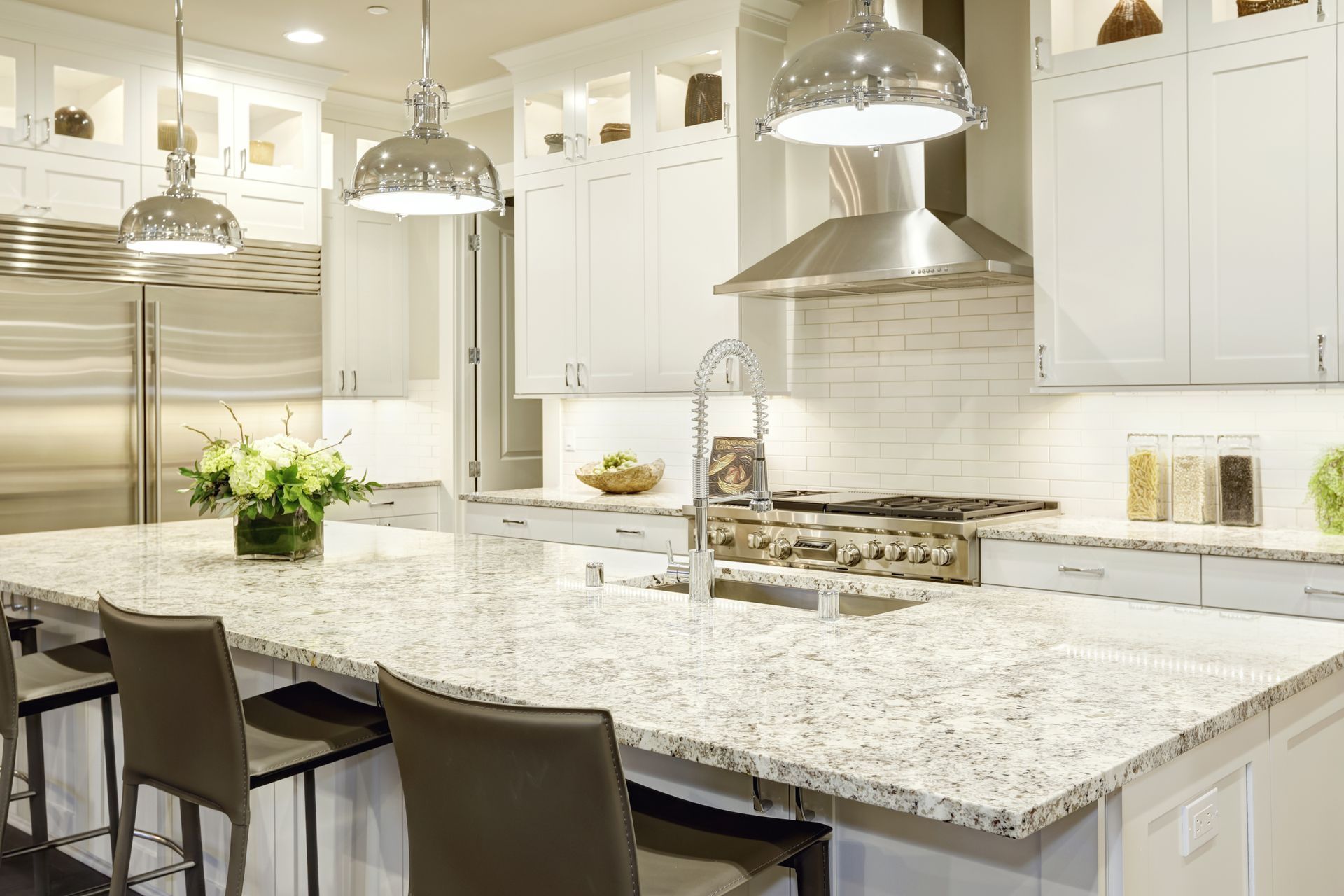 Bright white kitchen with granite countertops, stainless steel appliances, and island with bar stools.