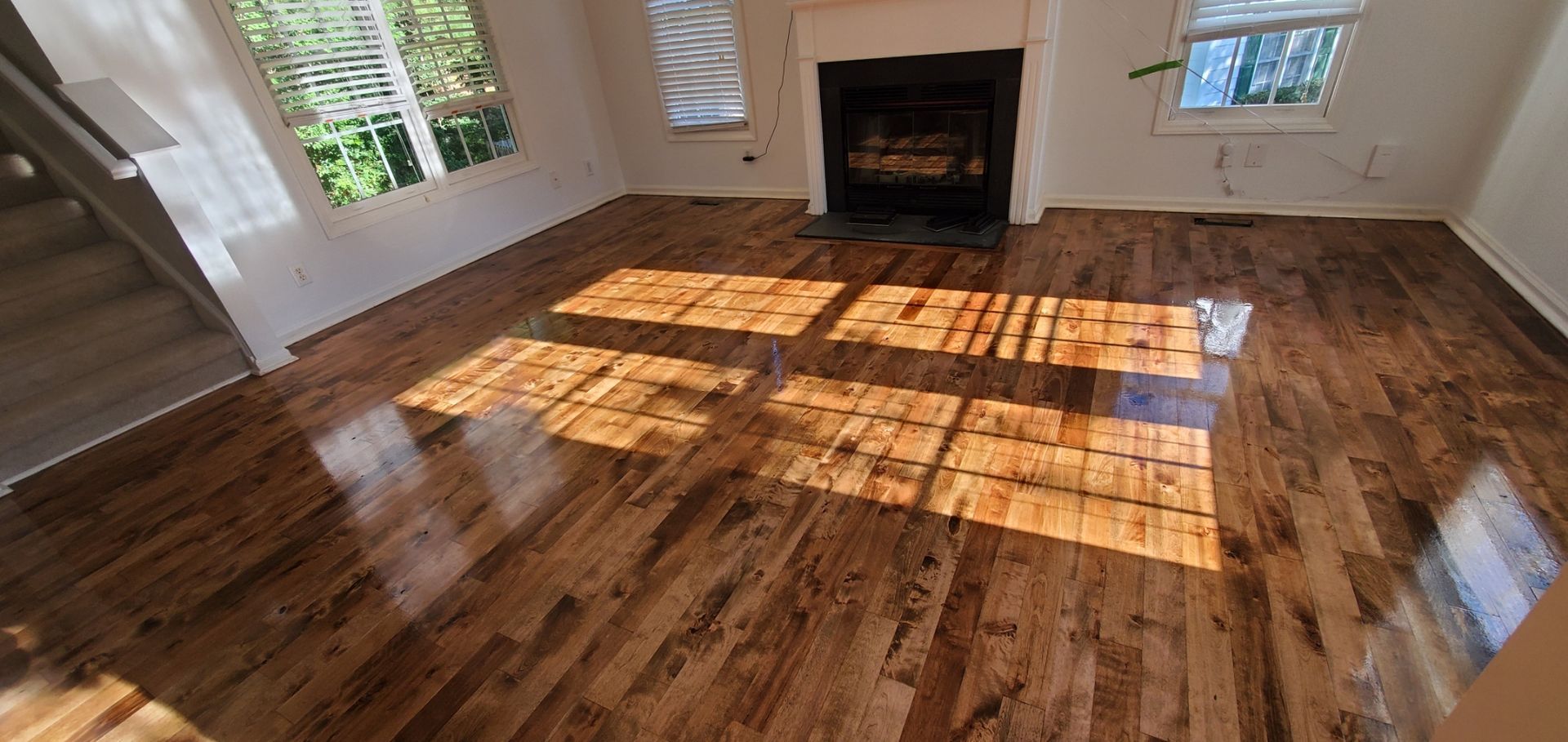 Sunlit hardwood floor in a room with a fireplace and windows.