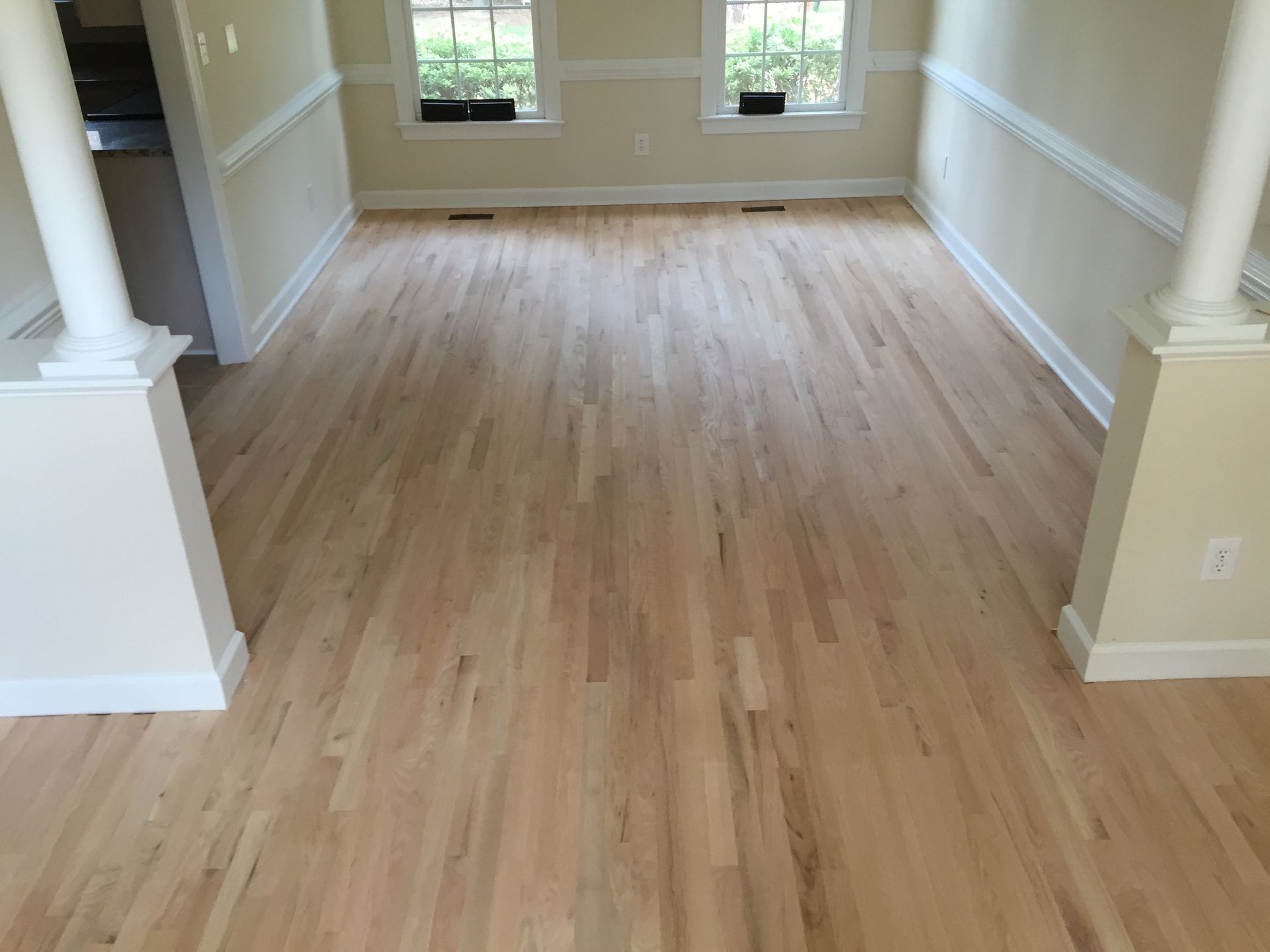 Newly installed light wood floor in an empty room with white columns, windows, and pale yellow walls.
