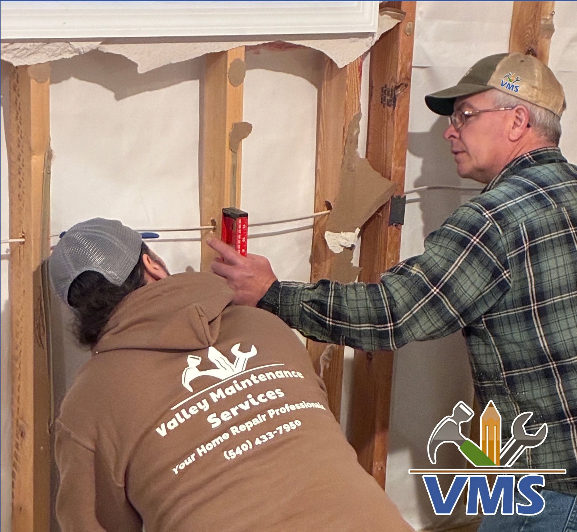 Workers inspecting a wall cavity during home repair, one holding a flashlight and one using a caulk gun