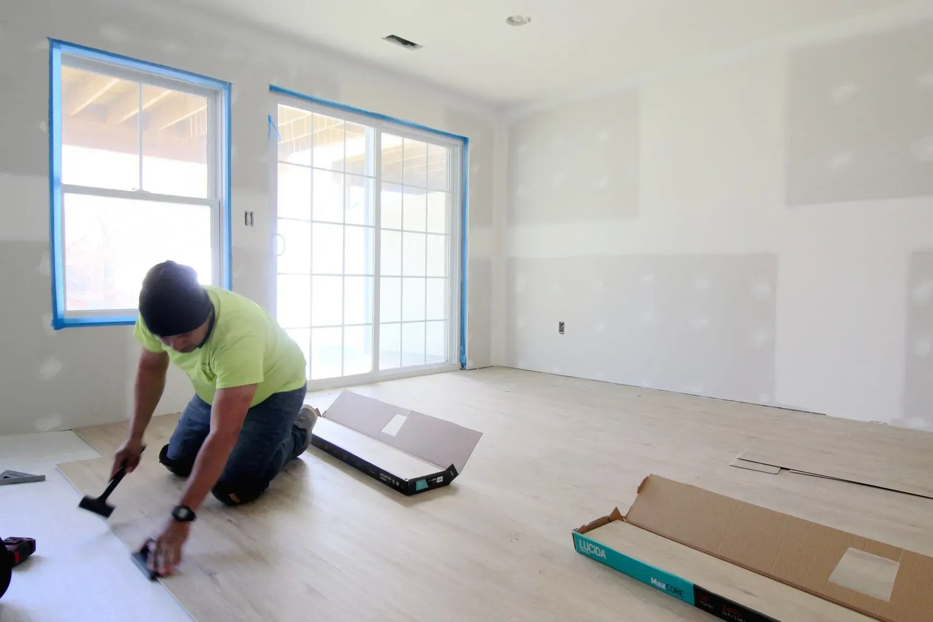 Person kneeling and assembling furniture in a bright, unfinished room with windows and boxes nearby