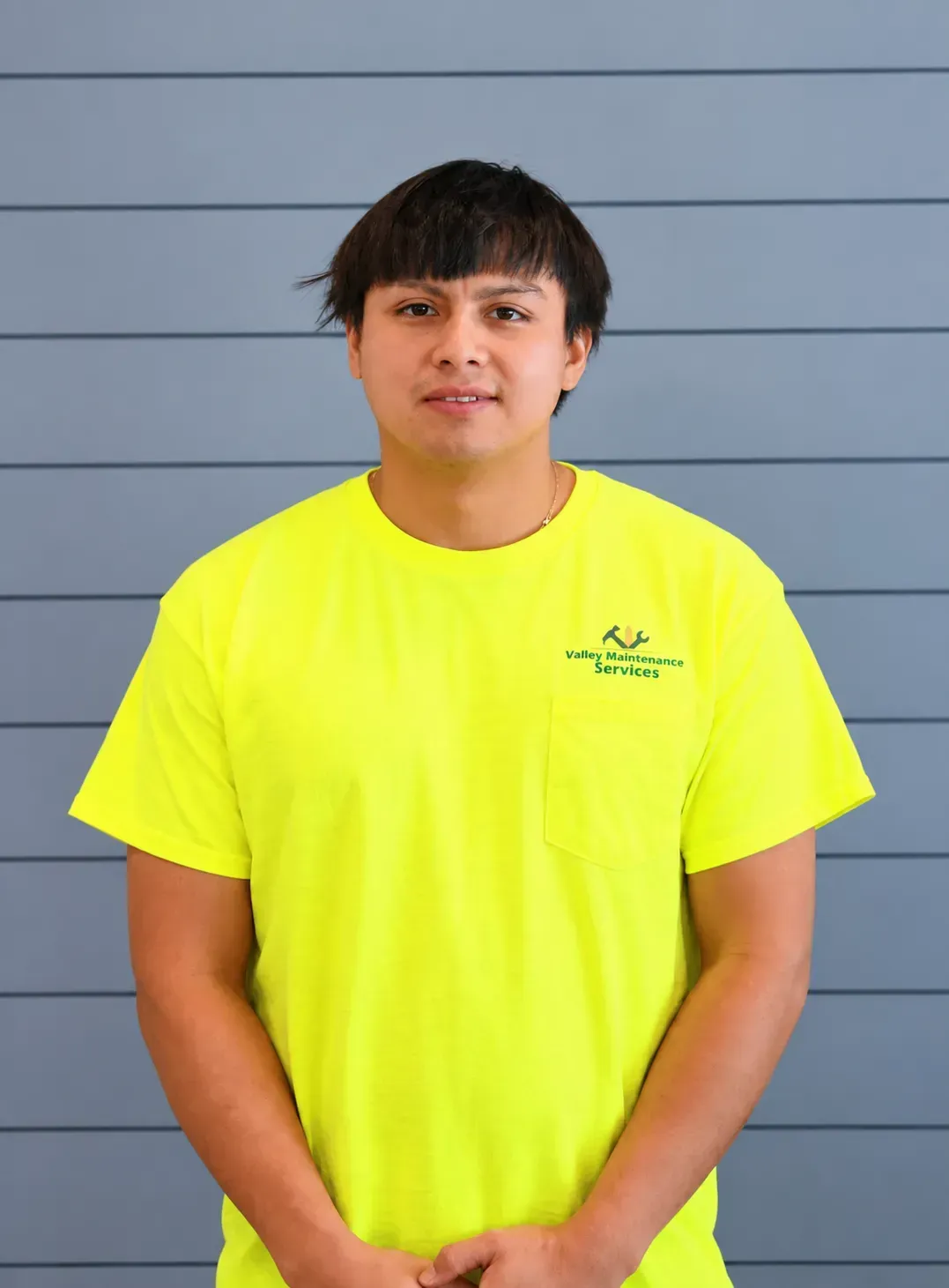 Person standing against a gray wall, wearing a bright yellow T-shirt and black pants.