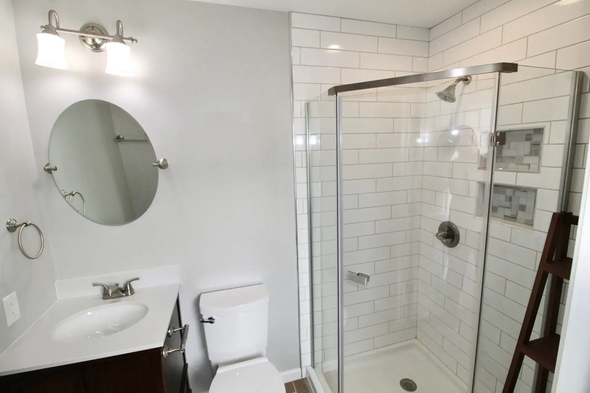 Bright bathroom with white subway tile, glass shower, sink, toilet, and round mirror