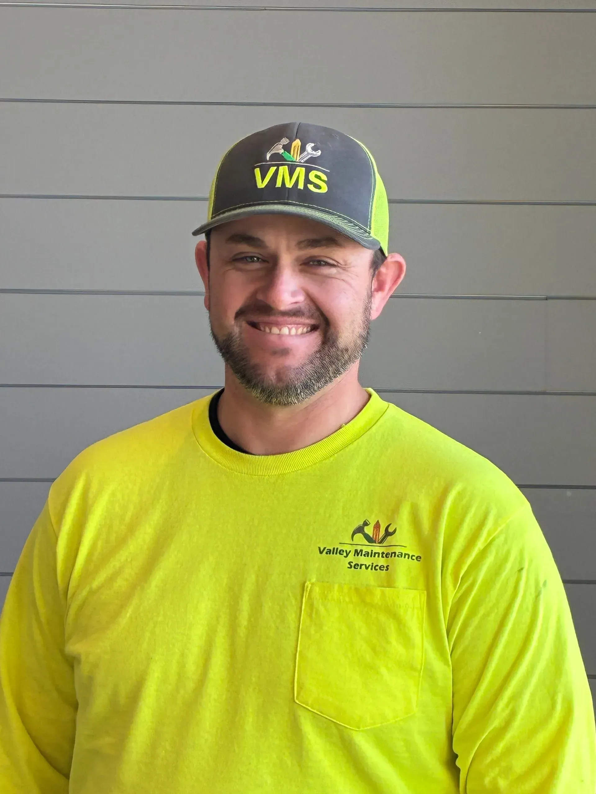 Smiling man in neon yellow shirt and VMS cap standing against a gray wall