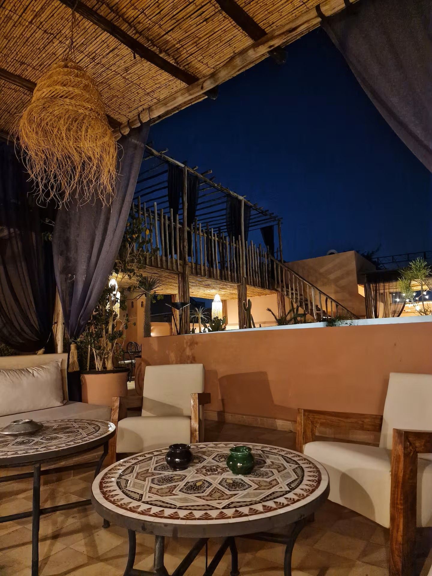 Terrasse sur le toit accueillante le soir, avec tables et chaises en mosaïque à motifs et éclairage d'ambiance chaleureux.