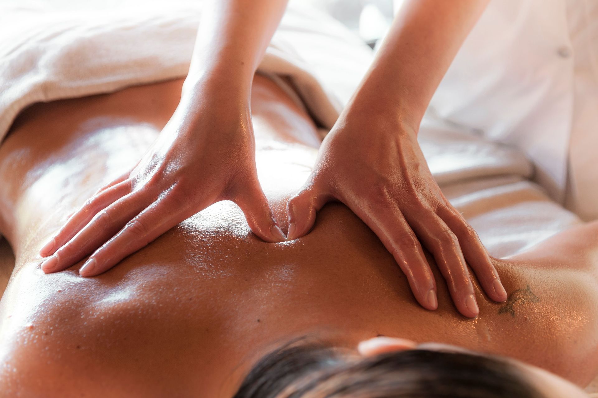 Les mains d'un masseur appliquant de l'huile sur le dos nu d'une personne
