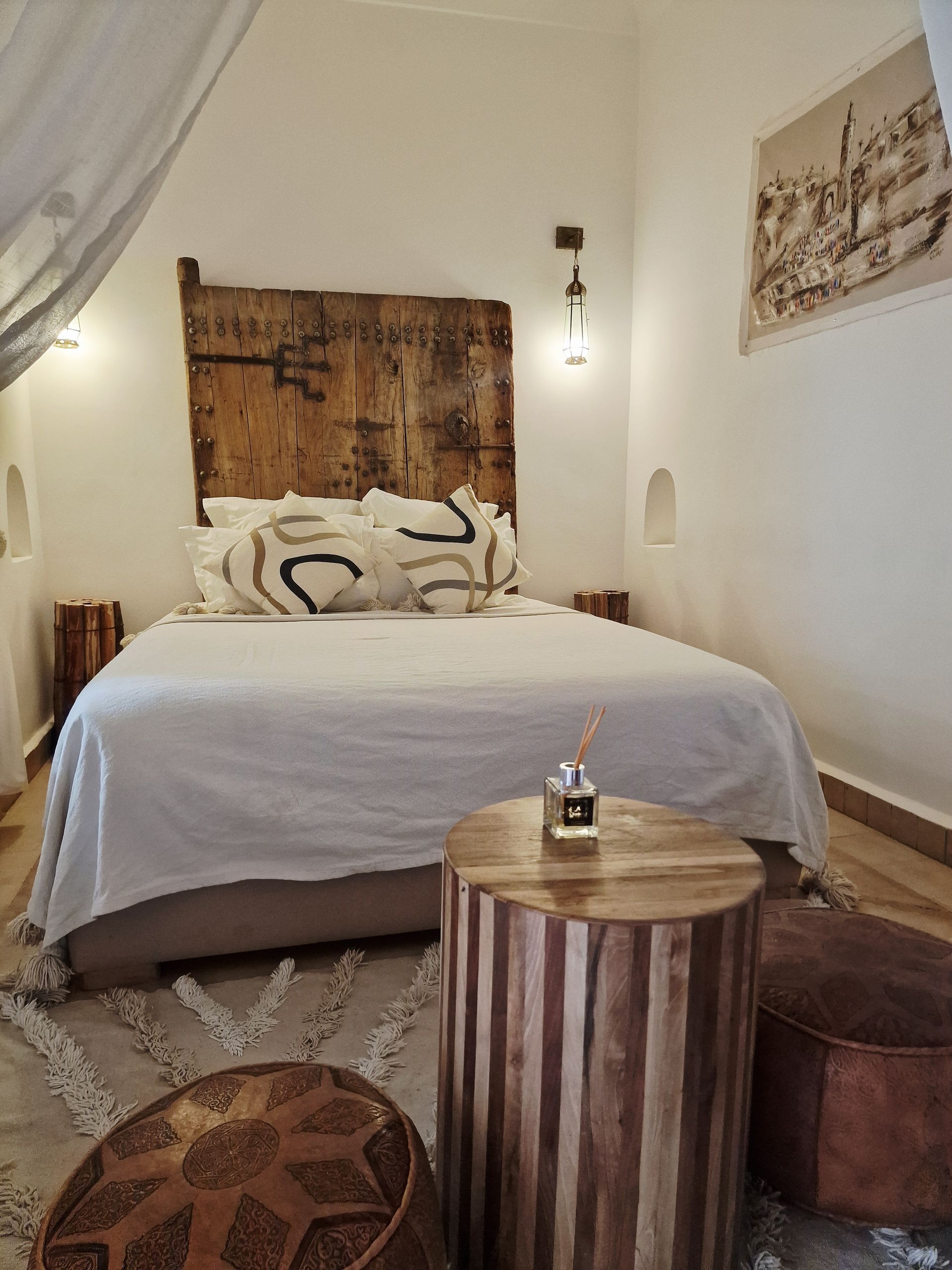 Chambre confortable avec un lit, des coussins à motifs, une table ronde en bois et une décoration neutre.