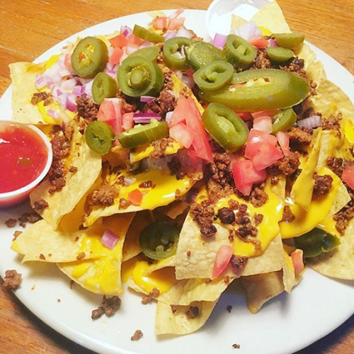 A white plate topped with nachos with tomatoes jalapenos and cheese