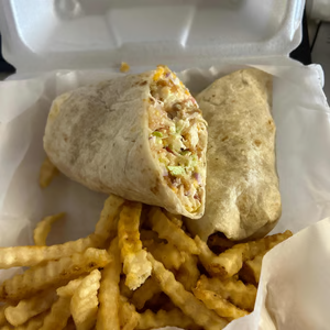A wrap and french fries are in a styrofoam container.
