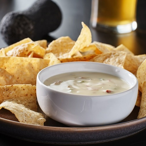 A bowl of dip sits on a plate of tortilla chips