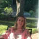 Woman seated outdoors in a pink floral top, lit by sunlight in a garden setting