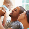Parent kissing baby while another adult smiles nearby on a couch