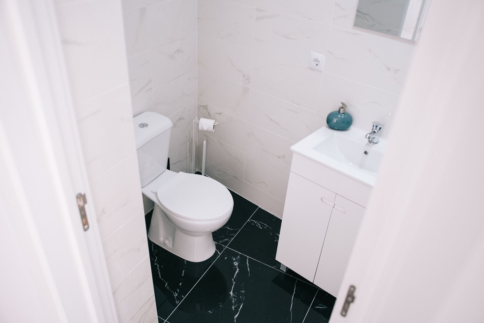 Small white bathroom with a toilet, vanity sink, and dark marble-pattern floor tiles.