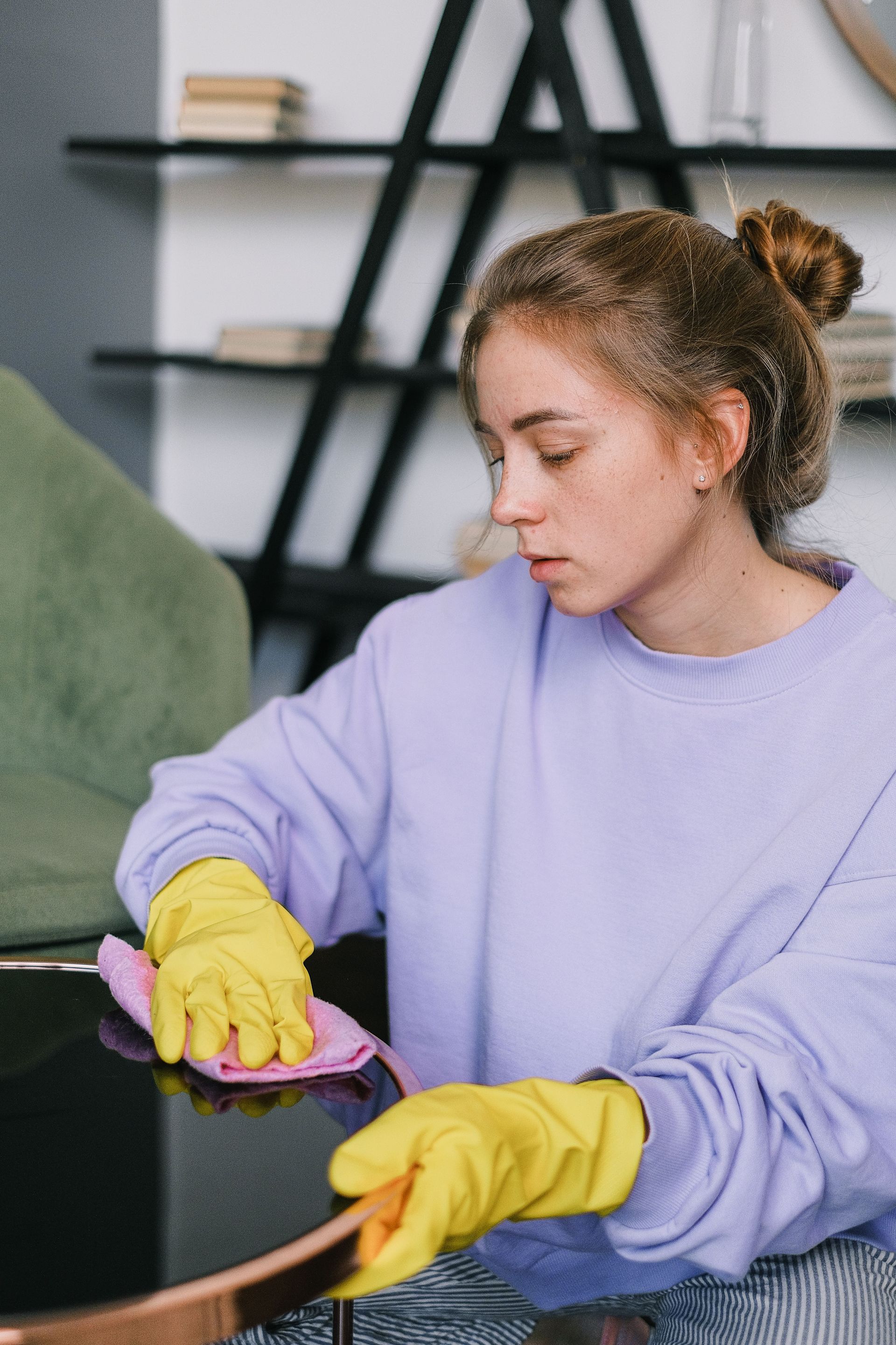 Person in yellow gloves cleaning a black table with a purple cloth, wearing a lavender sweatshirt.