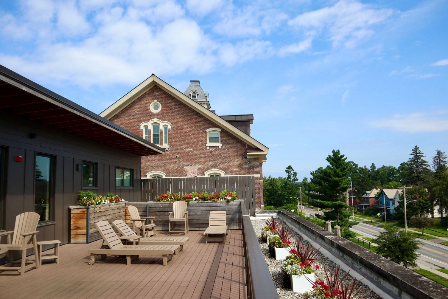 A rooftop deck with chairs and flowers in front of a brick building.