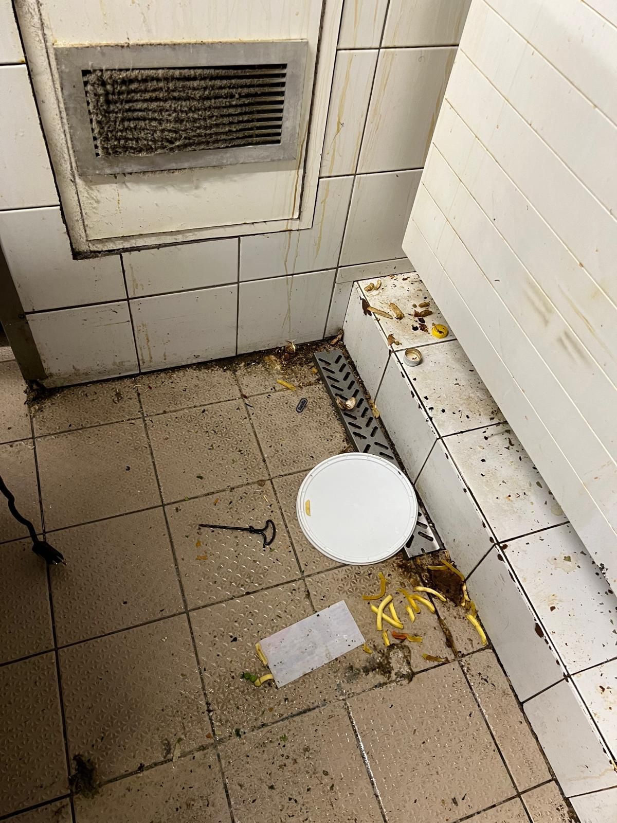 Une salle de bain sale avec un seau blanc sur le sol.