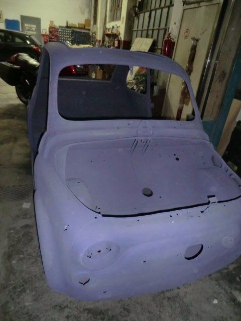 Carrozzeria di un'auto d'epoca, verniciata con primer viola, in un'officina, priva di finestrini e finiture.