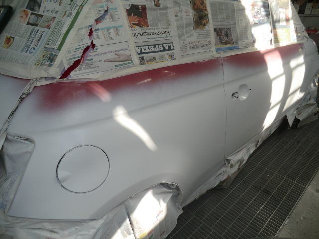 Un'auto in fase di riverniciatura in carrozzeria, coperta con giornali e primer sotto luci intense.
