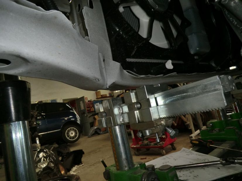 Primo piano di un assemblaggio meccanico metallico con bulloni e tubi in un'officina, con un'auto sullo sfondo.
