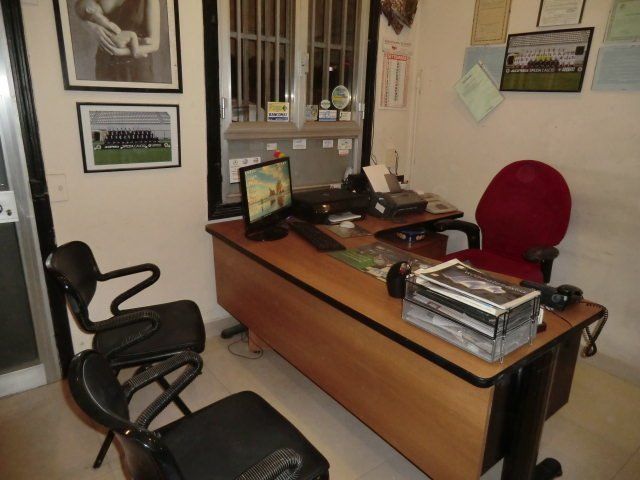 Ufficio con scrivania in legno, sedia nera, sedia rossa per gli ospiti e quadri incorniciati alle pareti.