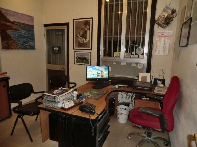 Piccolo ufficio con scrivanie, un computer, una sedia rossa e un quadro incorniciato appeso alla parete vicino a una finestra.