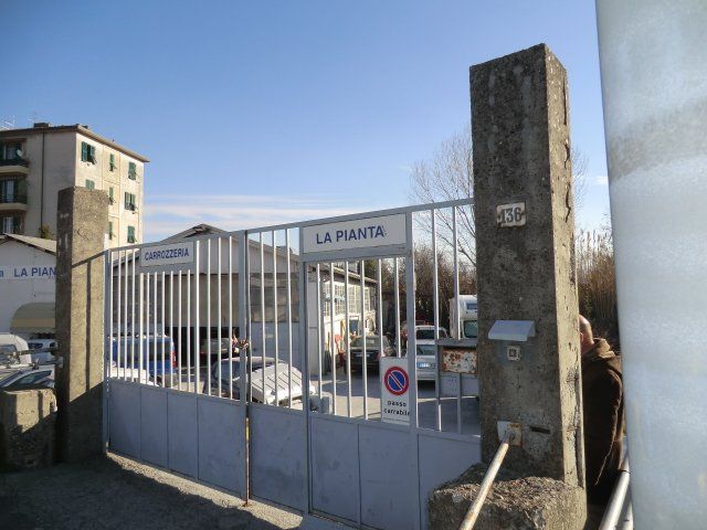 Ingresso recintato del complesso residenziale La Pianta con auto parcheggiate e pilastri in pietra sotto un cielo limpido
