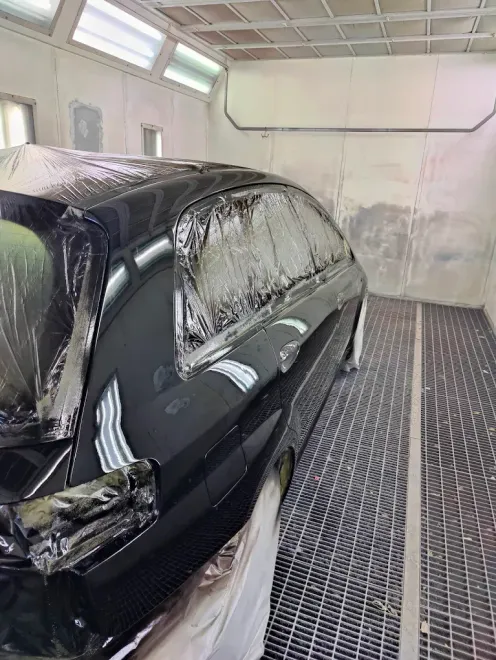 Auto nera in cabina di verniciatura, ricoperta di plastica e pellicola protettiva in attesa della riverniciatura.
